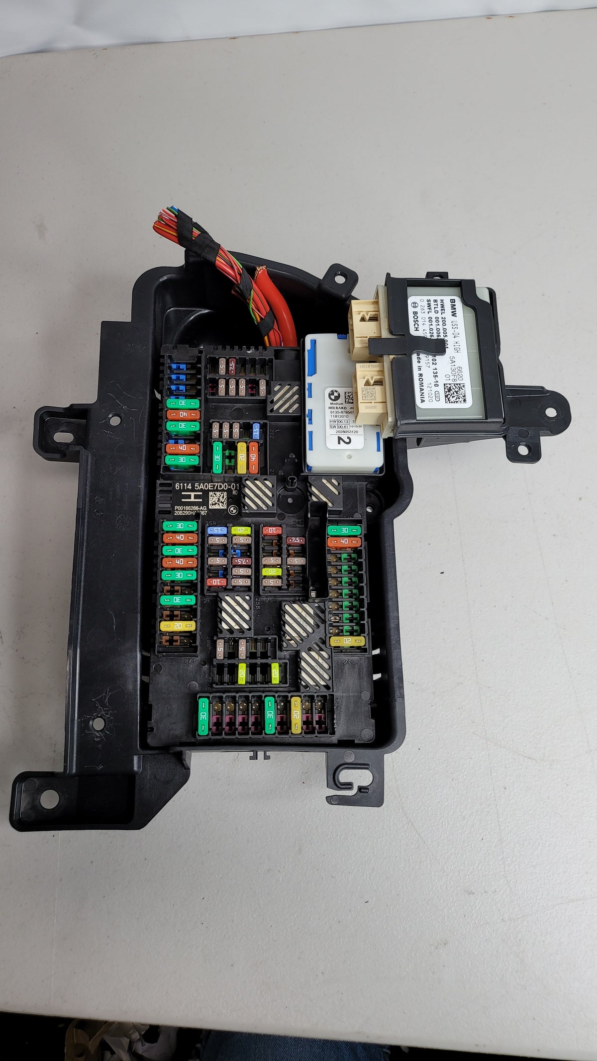 BMW M4 rear trunk power distribution fuse box, part 5A0E7D0, with visible fuse slots and wiring for engine compartment.