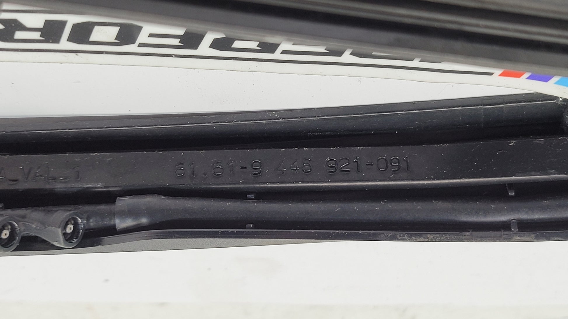 BMW M3 G8x passenger side front wiper arm by MPerformance.parts with metal and plastic components, mounted on vehicle windshield.